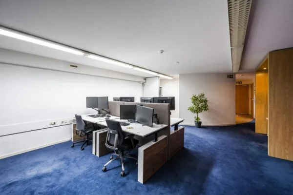 Moderne kantoorruimte aan de Prins Hendrikkade met werkplekken, bureaustoelen en meerdere computerschermen op een blauw tapijt.